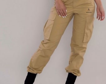 May include: A pair of khaki cargo pants with a belt and a logo that says "MAWAZI". The pants have multiple pockets and a cuffed hem.