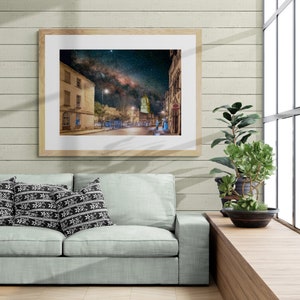 May include: A framed photograph of a city street at night with the Milky Way visible in the sky. The street is lined with buildings and streetlights.