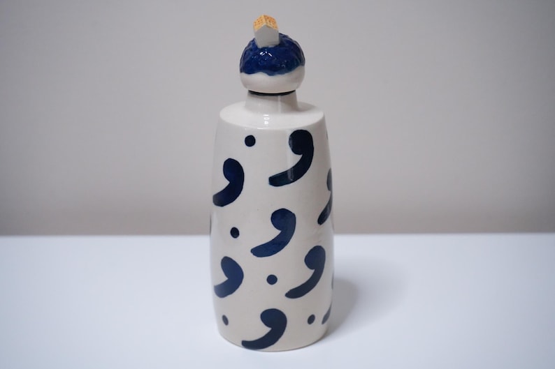 May include: A white ceramic bottle with a dark blue comma pattern and a dark blue and white stopper. The bottle has a cylindrical shape and is suitable for storing liquids. The stopper is made of ceramic and cork.