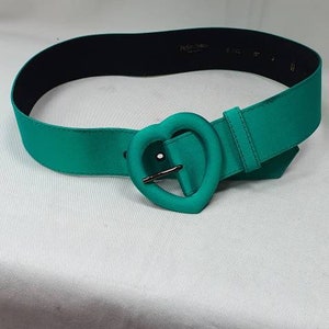 May include: A teal satin belt with a heart-shaped buckle. The buckle is made of metal and has a shiny finish.