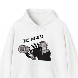 May include: White hooded sweatshirt with a black and white graphic print of a hand holding a telescope with the text "Thee Oh Sees" above the graphic.