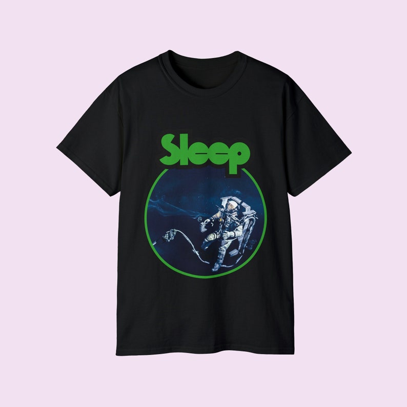 Pu&ograve; includere: Maglietta nera con un grafico circolare verde che presenta un astronauta nello spazio. Il testo "Sleep" &egrave; stampato in verde sopra il cerchio.