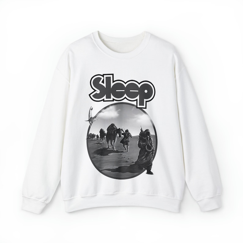 Op de afbeelding: Witte longsleeve sweatshirt met een zwart-witte grafische print van een band genaamd "Sleep". De afbeelding toont een woestijnsc&egrave;ne met mensen en kamelen.