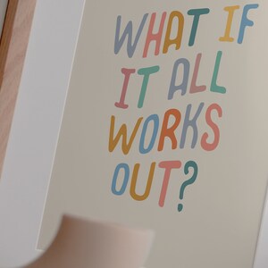 Puede incluir: Una impresi&oacute;n enmarcada con el texto "What if it all works out?" en letras escritas a mano de colores sobre un fondo beige.