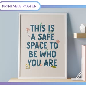 May include: A printable poster with a white frame and a light pink background. The poster features the text "This is a safe space to be who you are" in blue lettering with floral illustrations.