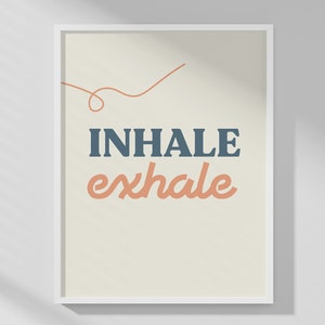 May include: A framed art print with the words "INHALE exhale" in blue and peach-colored text. The words are centered on a cream-colored background, with a thin orange line above the word "INHALE". The print is in a white frame.
