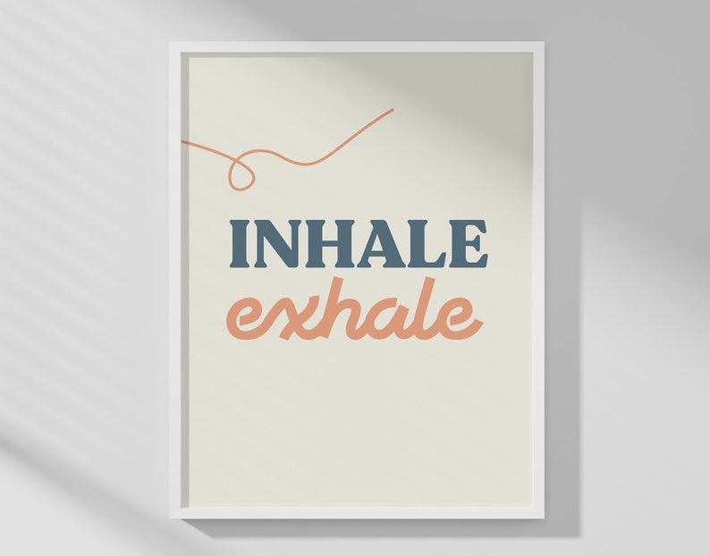 May include: A framed art print with the words "INHALE exhale" in blue and peach-colored text. The words are centered on a cream-colored background, with a thin orange line above the word "INHALE". The print is in a white frame.