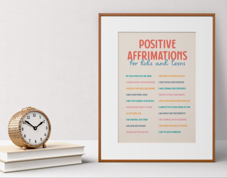 May include: A framed print with the text "POSITIVE AFFIRMATIONS for kids and teens" in red and blue. A gold-colored woven clock sits on a stack of books to the left of the print.