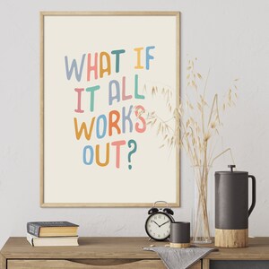 Puede incluir: Una impresi&oacute;n enmarcada con el texto "What if it all works out?" en letras escritas a mano de colores sobre un fondo crema. La impresi&oacute;n est&aacute; colgada en una pared blanca sobre una mesa de madera con un jarr&oacute;n de avena seca, un reloj y una cafetera.