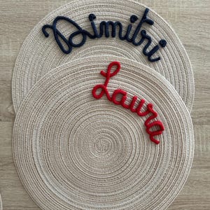 Può includere: Due tovagliette all'uncinetto con i nomi "Dimitri" e "Laura" ricamate in filo nero e rosso.
