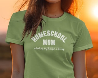 May include: A light green t-shirt with the text "HOMESCHOOL MOM" in a white, arched font. Below, the text reads "schooling my kids for a living". The shirt is worn against a blurred sunset backdrop.