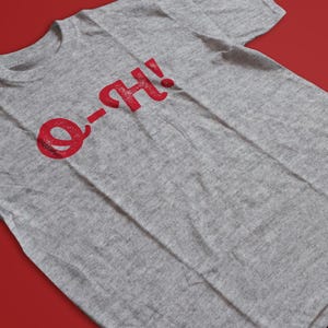 May include: A heather gray t-shirt with the red text "O-H!". The text is in a distressed, vintage style. The shirt is displayed on a red background.