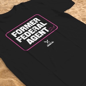 May include: Black t-shirt with a pink rectangle that says "FORMER FEDERAL AGENT" in white text. The text "Ex-Special Agent" is written in cursive in the top right corner of the rectangle. The text "SHORTY FX" is written in white text below the rectangle.