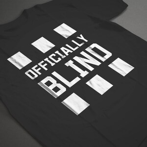 May include: Black t-shirt with white text that reads "Officially Blind" with a pattern of white squares behind the text.