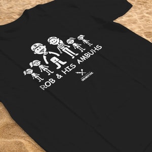 Può includere: Maglietta nera con una grafica bianca di una famiglia con il testo "Rob & His Ambuhs".