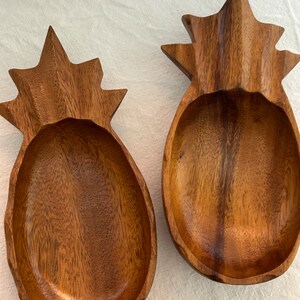 May include: Two wooden pineapple-shaped bowls. The bowls are made of dark brown wood and have a carved pineapple design.