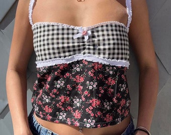 May include: A black and white gingham tank top with a white lace trim and a pink bow. The top has a floral print on the bottom half.