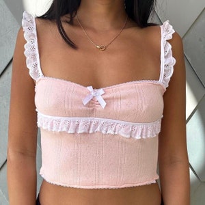 May include: A pink crop top with white lace trim and a bow at the neckline.
