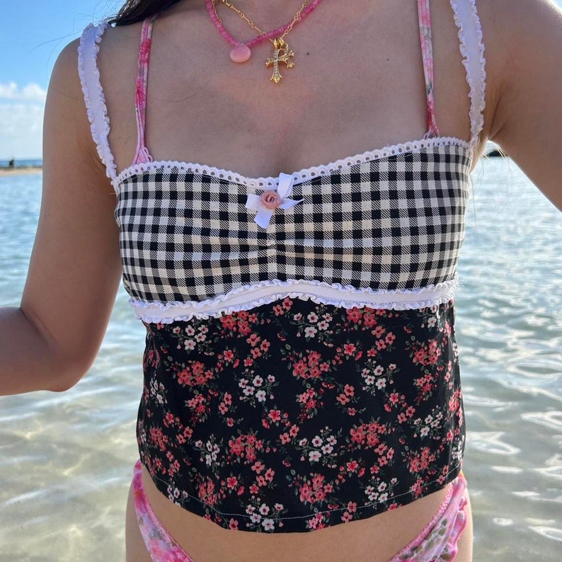 May include: A black and white gingham tank top with a floral print bottom. The top has a white lace trim and a pink bow with a small flower detail.