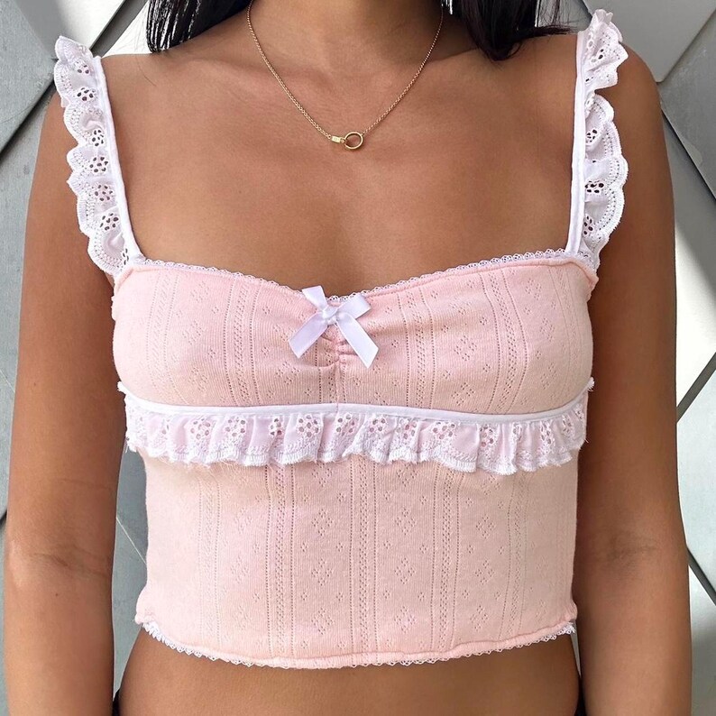 May include: A pink crop top with white lace trim and a bow at the neckline.