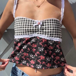 May include: A black and white gingham top with a floral print bottom. The top has a white lace trim and a pink bow in the center. The top is cropped and has a sweetheart neckline.