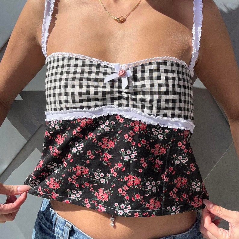 May include: A black and white gingham top with a floral print bottom. The top has a white lace trim and a pink bow in the center. The top is cropped and has a sweetheart neckline.