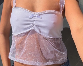 May include: White crop top with a lace overlay and a bow detail. The top has a fitted bodice and a loose, flowing bottom.