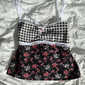 May include: A black and white gingham top with a floral print skirt. The top has white lace trim and a pink bow. The skirt has a white lace trim.