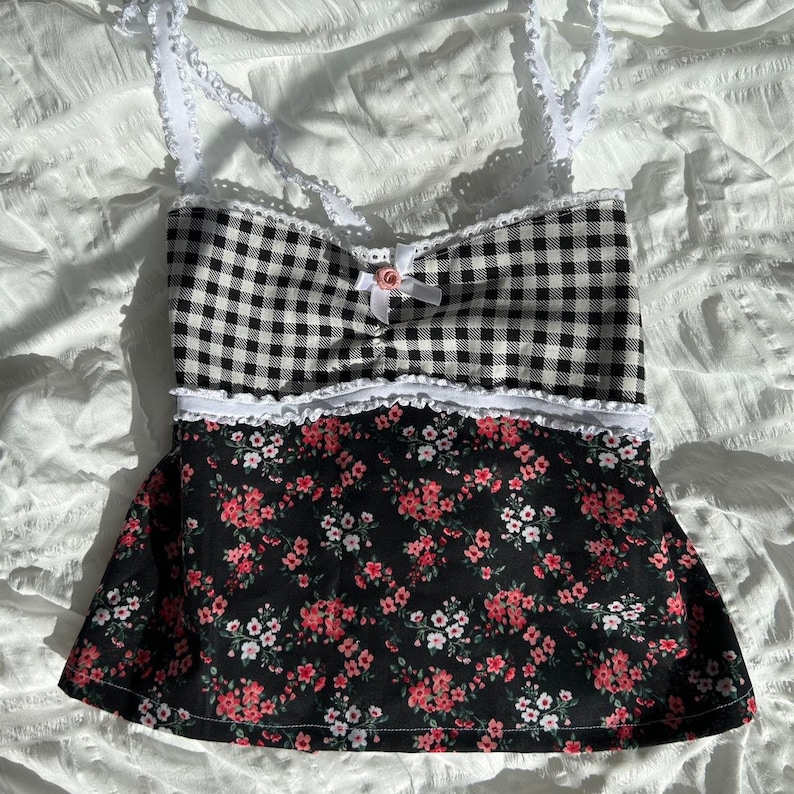 May include: A black and white gingham top with a floral print skirt. The top has white lace trim and a pink bow. The skirt has a white lace trim.