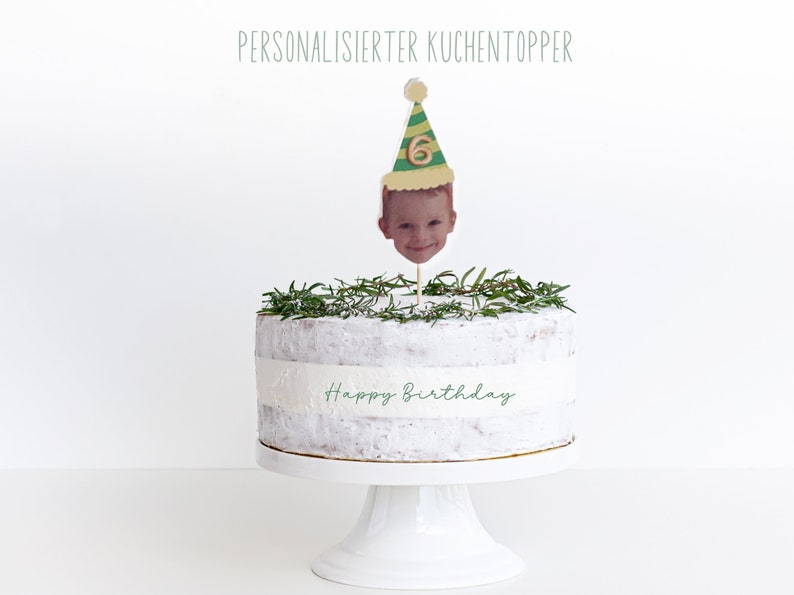 Puede incluir: Un pastel blanco decorado con ramitas de romero verde y un adorno de pastel personalizado. El adorno presenta la cara de un ni&ntilde;o con un gorro de fiesta verde y amarillo con el n&uacute;mero 6. El pastel est&aacute; decorado con las palabras "Feliz cumplea&ntilde;os".