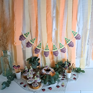 Puede incluir: Una decoraci&oacute;n de fiesta de cumplea&ntilde;os con una pancarta de fotos de ni&ntilde;os con gorros de fiesta. La pancarta est&aacute; colgada en una pared decorada con serpentinas de papel de seda de color melocot&oacute;n y crema. Hay cupcakes con glaseado y chispas en una mesa delante de la pancarta.