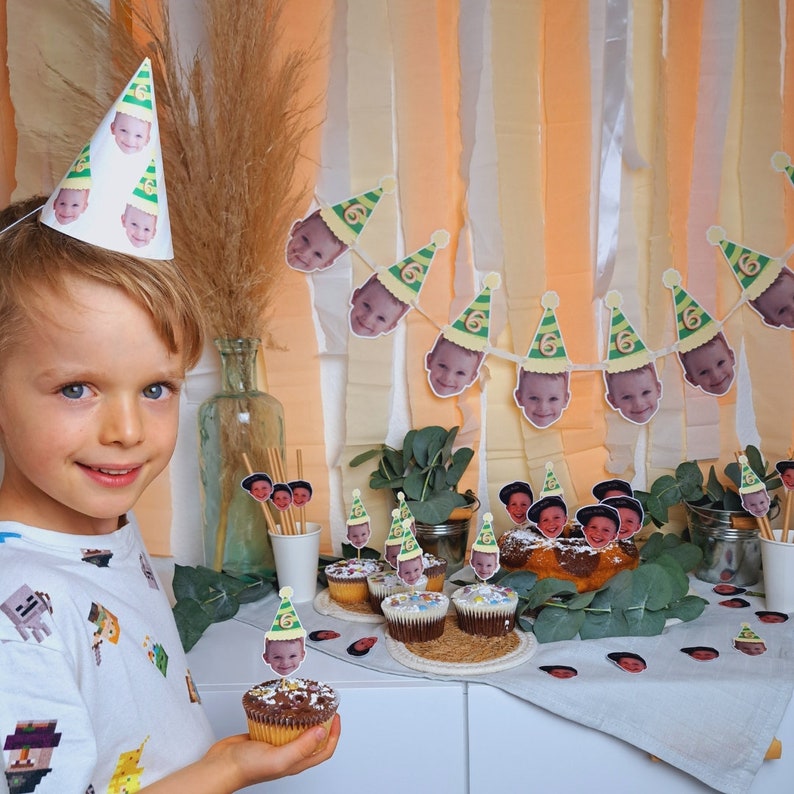 Puede incluir: Una mesa de fiesta de cumplea&ntilde;os con cupcakes decorados con sombreros de fiesta verdes y amarillos con fotos de caras de ni&ntilde;os. La mesa est&aacute; cubierta con un mantel blanco con una guirnalda verde de sombreros de fiesta con fotos de caras de ni&ntilde;os. Tambi&eacute;n hay peque&ntilde;os frascos llenos de caramelos de colores.