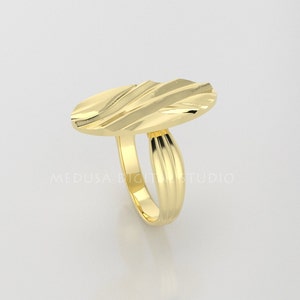 Pu&ograve; includere: Un anello d'oro con una parte superiore ovale testurizzata. La fascia &egrave; anche testurizzata con linee verticali.