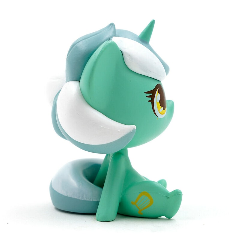 May include: A figurine of a seated, stylized pony with a light teal body, blue mane and tail, and white accents. The pony has a yellow harp symbol on its leg and a single horn. The eyes are large and detailed.