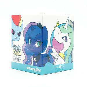 May include: A cube-shaped box featuring cartoon illustrations of My Little Pony characters. The box has a light blue base and the text "Studio Chibi" and "we love fine" are visible. The box is part of the "Fan Favorites Collection".