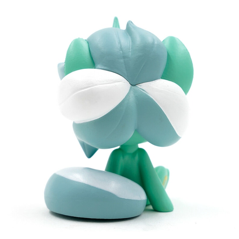 May include: A small, stylized figurine in shades of teal, white, and green. The figure has a large, flower-like head with white and teal petals. It is seated with a rounded teal base. The figurine is on a white background.