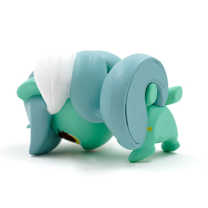 May include: A turquoise figurine of a stylized animal, possibly a ram or sheep, with large curved horns and a white patch on its back. The figurine is lying on its side, showcasing its rounded form and simple design.