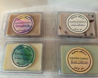 Puede incluir: Cuatro recipientes rectangulares de cera aromática en envases de plástico transparente. Cada uno tiene una etiqueta circular que dice "Handmade with love", "SCENTED CANDLE" y "Just for you". Los aromas son Almond Macaron, Love Spell, Clean Cotton y Blue Spruce.