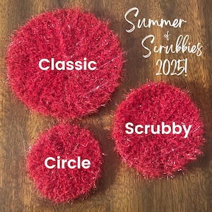 May include: Three red, circular scrubbies with the words "Classic", "Scrubby", and "Circle" in white text. The image also includes the text "Summer of Scrubbies 2025!" in a cursive font. The scrubbies are on a wooden surface.