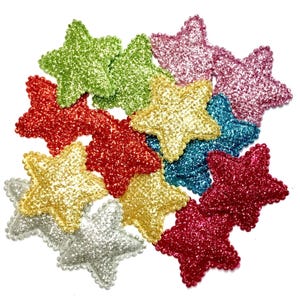May include: A collection of star-shaped patches featuring a dense, glittery texture. The assortment includes multiple colours such as lime green, bright red, gold, silver, teal, magenta, and pink, all arranged in a clustered, overlapping formation.