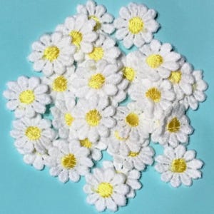 May include: A collection of small, circular embroidered daisy patches featuring white petals and a bright yellow centre. Each patch is crafted with detailed stitching, creating a textured floral design suitable for various textile applications.