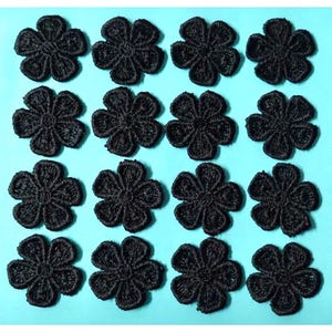 May include: A collection of sixteen identical black embroidered flower patches arranged in a four-by-four grid. Each patch features a five-petaled floral design with detailed stitching, creating a textured surface on each individual flower shape.
