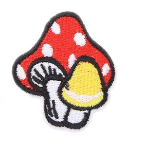 May include: An embroidered patch featuring a large red mushroom cap with white spots, layered over a smaller white mushroom with black gills and a separate yellow-capped mushroom, all outlined with a thick black border on a white background.