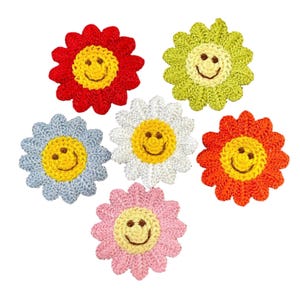 May include: A collection of six crocheted flower appliqués, each featuring a central yellow face with a stitched brown smiley expression. The petals are rendered in distinct solid colours including red, lime green, light blue, white, orange, and pink.