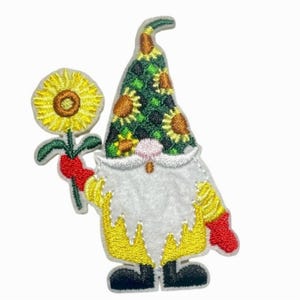 May include: An embroidered patch featuring a gnome wearing a green hat patterned with sunflowers. The gnome has a long white beard, a yellow tunic, red gloves, and black boots. It holds a large yellow sunflower with a brown centre on a green stem.