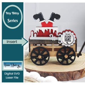 May include: A wooden toy wagon with a red and white Santa Claus figure hanging upside down from the top. The wagon has black wheels and a wooden frame. The wagon has a sign that says "Scan" with a QR code on it.