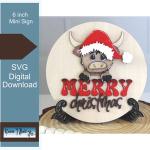 Puede incluir: Un letrero de madera de 15 cm de diámetro con una vaca de las Tierras Altas con un gorro de Papá Noel. El letrero dice "MERRY christmas" en letras rojas. Es una descarga digital SVG.