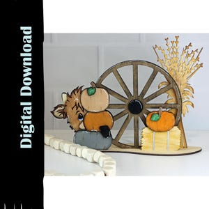 May include: Wooden fall-themed decoration featuring a cow, pumpkins, a wagon wheel, and wheat stalks. The cow has a light brown face and is stacked with two pumpkins. An orange pumpkin sits on a hay bale. The text "Digital Download" is on the left.
