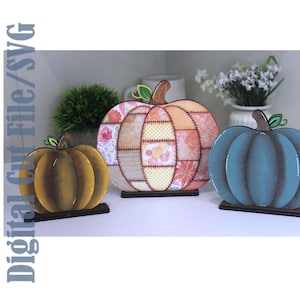 May include: Three decorative pumpkin cutouts with stands. The left is solid mustard yellow, the center features a patchwork floral pattern in peach and cream, and the right is a solid teal blue. The text Digital Cut File/SVG is visible.