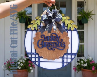 Pode incluir: Uma placa de porta redonda de madeira com uma moldura azul-escura em padrão de grade, uma placa central de madeira recortada com o texto azul-escuro Merry Christmas e um laço decorativo de fitas azul-marinho, brancas e bege com folhagem.
